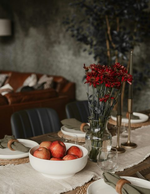 Mesa dispuesta con flores rojas, un cuenco de manzanas y velas