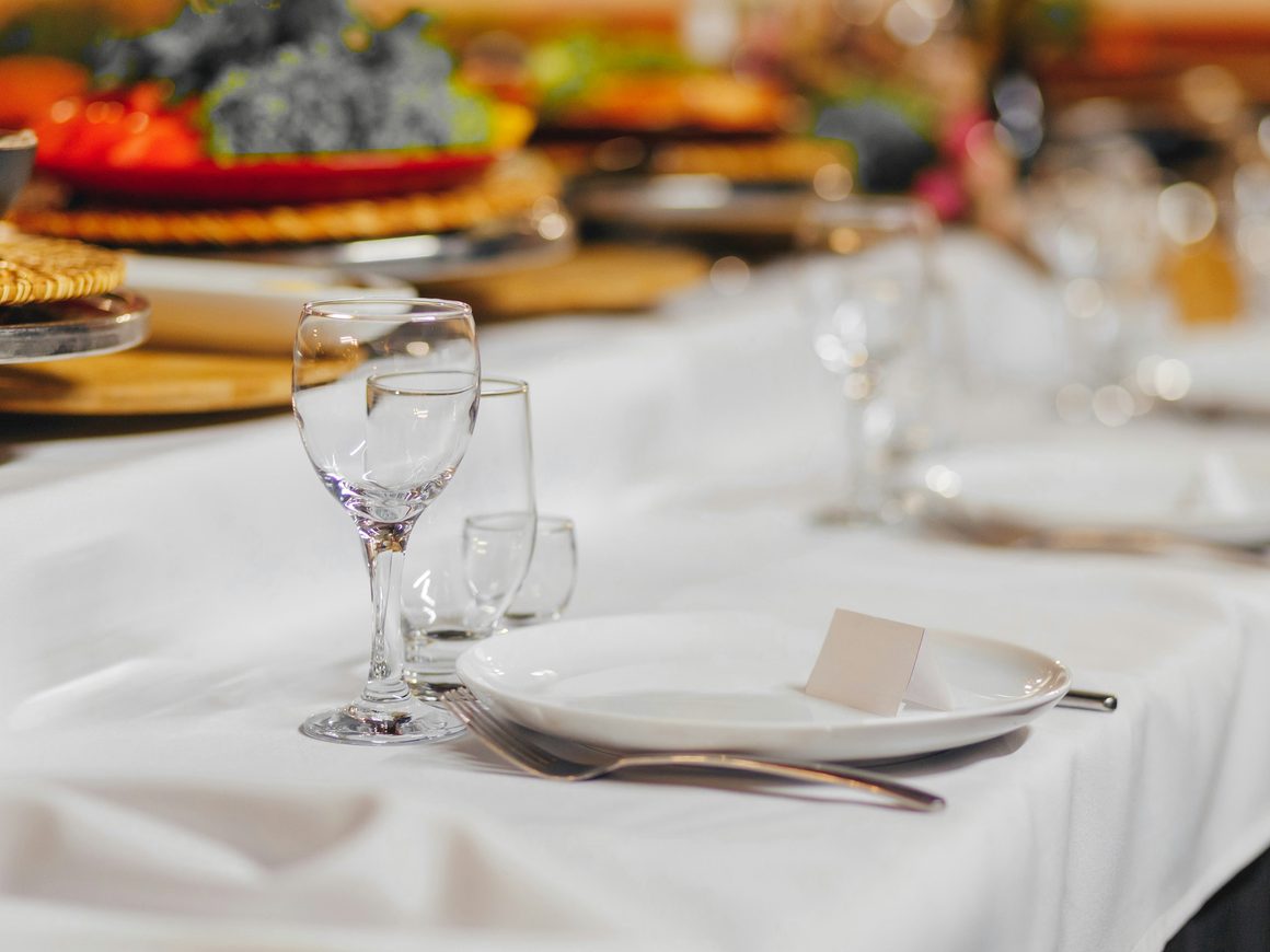 Mesa con mantel blanco servida con copas, platos y cubiertos
