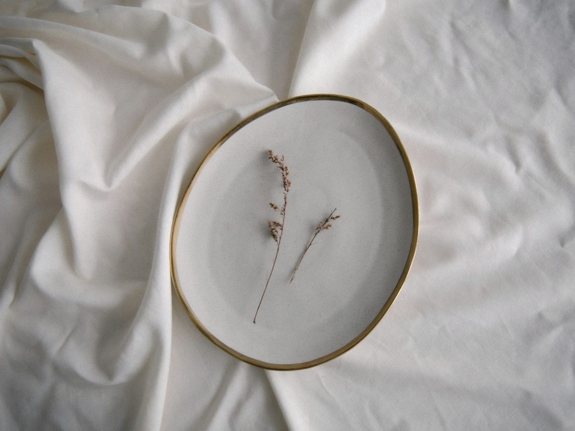 Plato de porcelana de borde irregular sobre una tela blanca, con una ramita seca