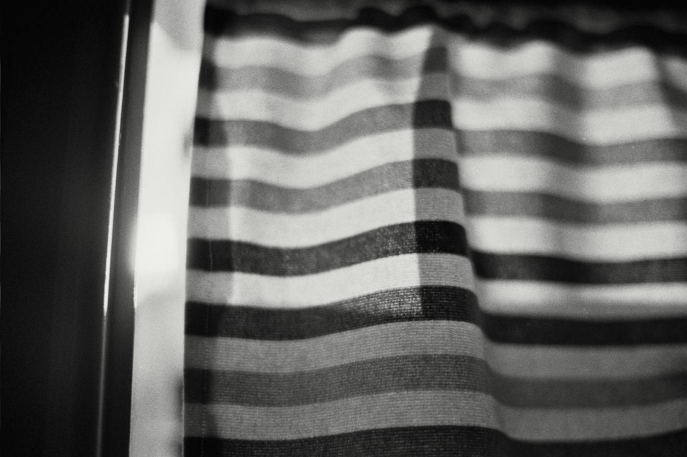 Una cortina a rayas con la luz de la ventana detrás, en blanco y negro