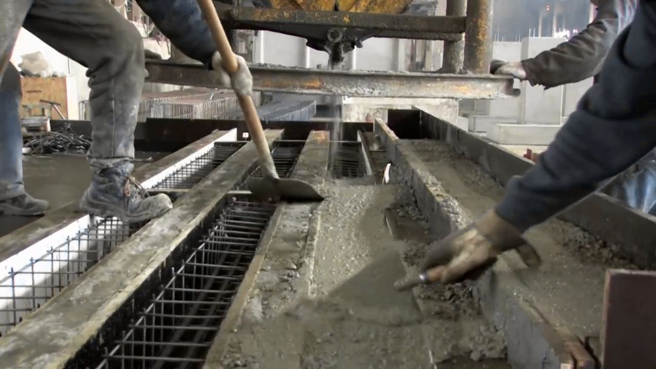 Obreros con botas y guantes extendiendo hormigón fresco sobre una malla de acero dentro de un encofrado