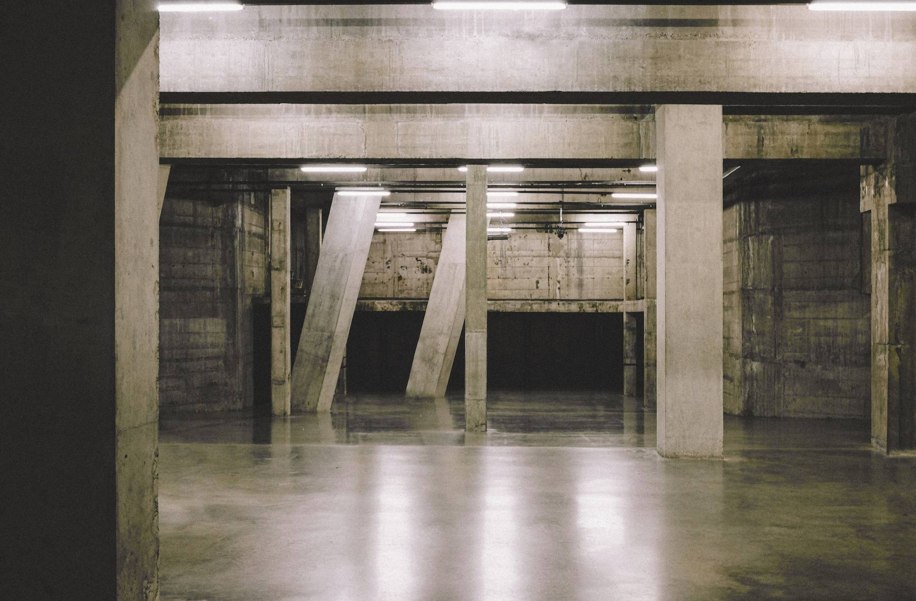 Nave de hormigón con columnas inclinadas, luces de tubo en el techo y un suelo pulido que refleja la luz
