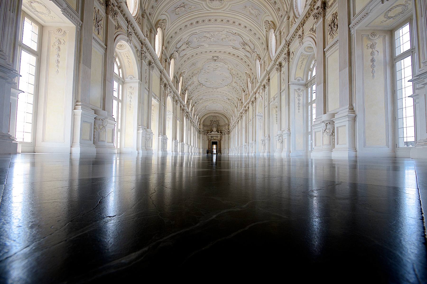 Sala larguísima con ventanales a los lados y un suelo negro pulido que refleja la luz