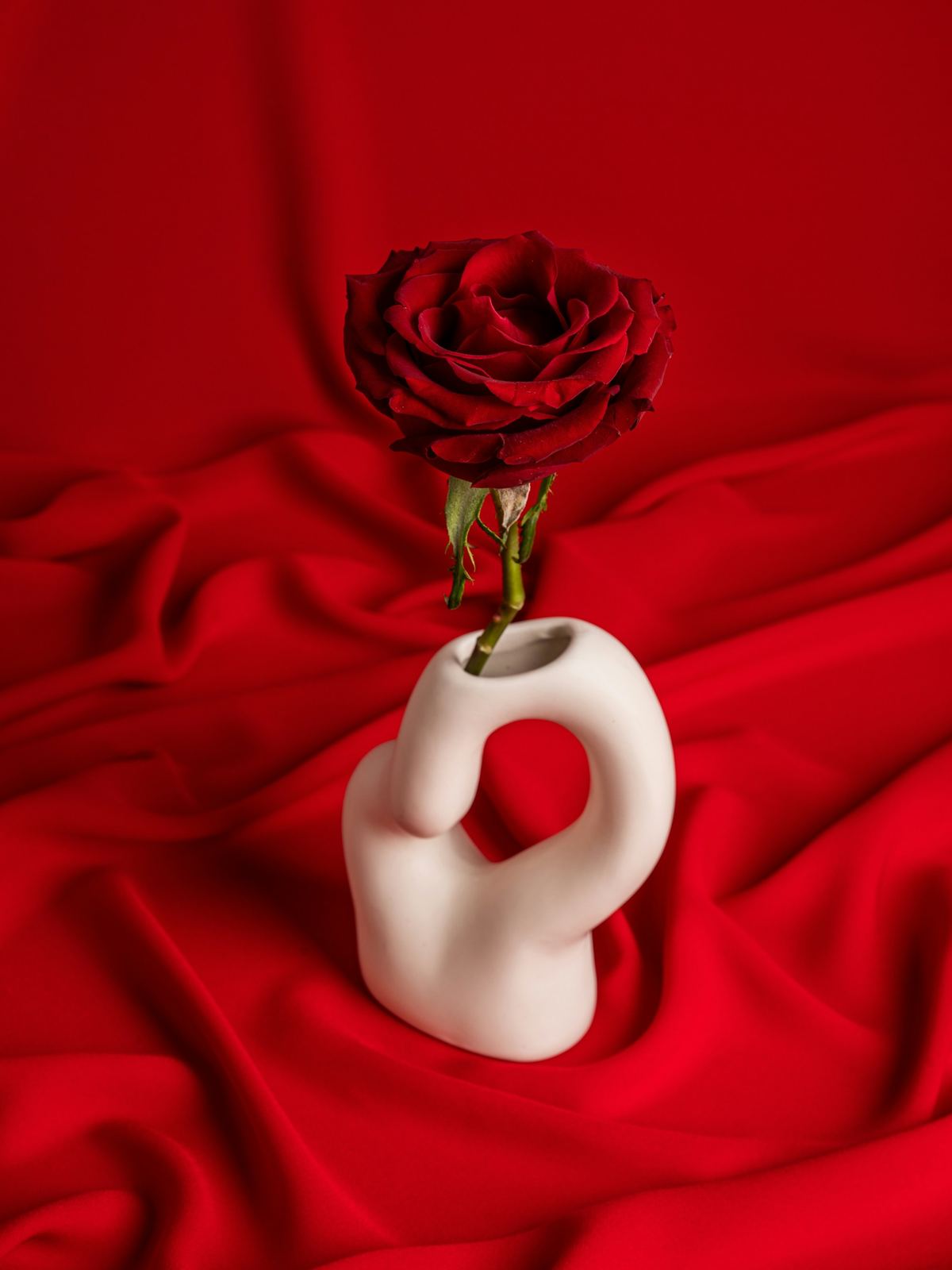 Jarrón de cerámica blanco con forma de nudo, sobre una tela roja