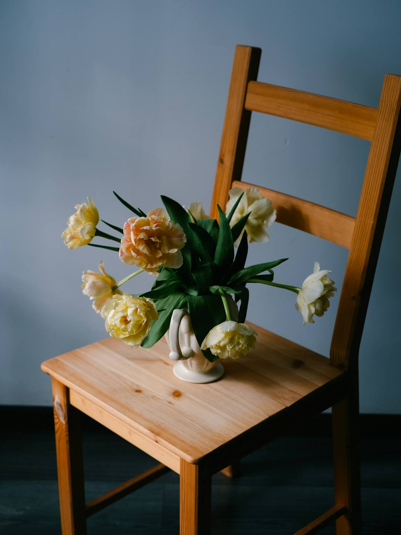 Silla de pino con un jarrón de tulipanes sobre el asiento, frente a una pared azul