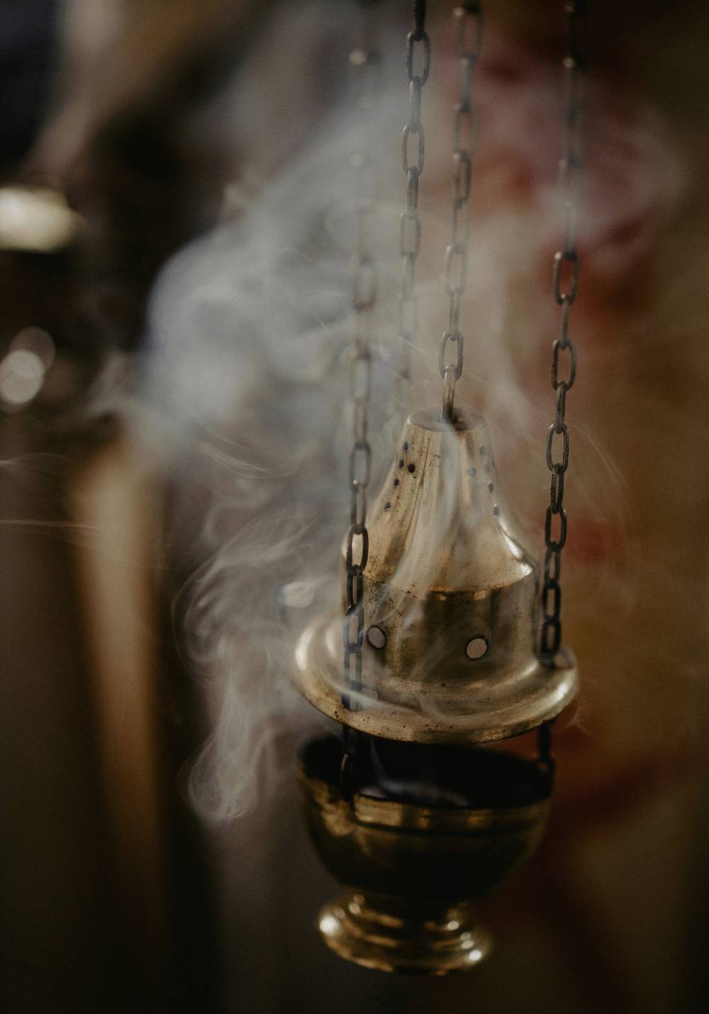 Un incensario de bronce colgado de cadenas, entre humo