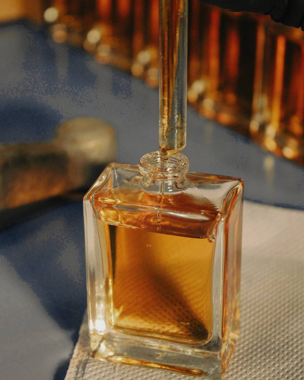 Un frasco de perfume ámbar bajo un gotero, con una fila de frascos detrás