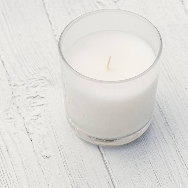 Una vela blanca en vaso de vidrio sobre una tabla clara