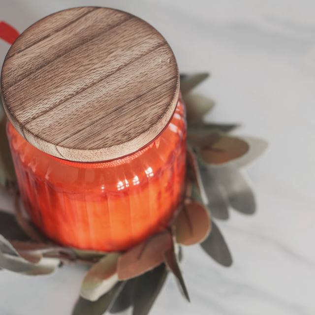 Una vela naranja en frasco con tapa de madera