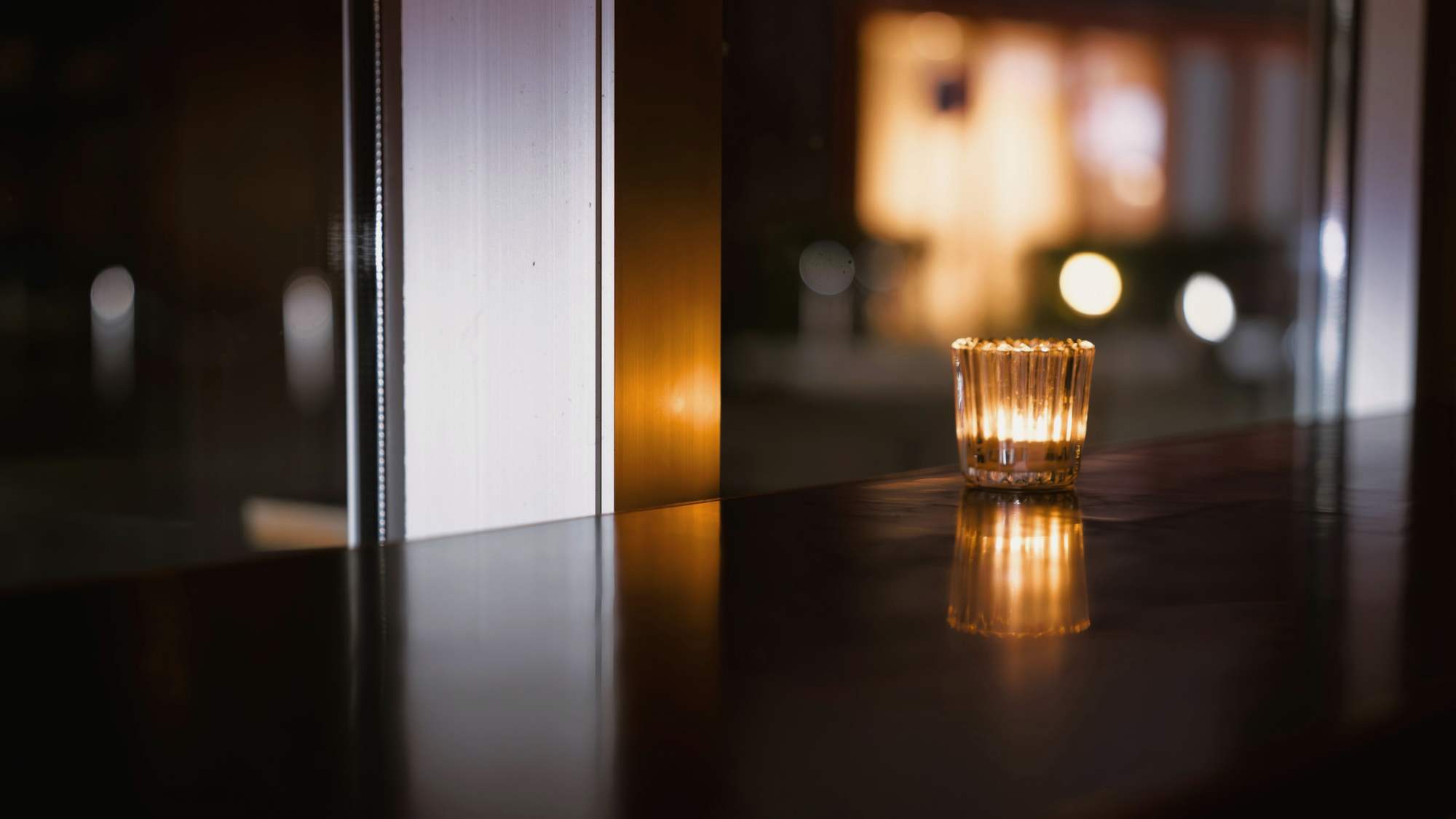 Una vela encendida sobre una mesa oscura de reflejos cálidos