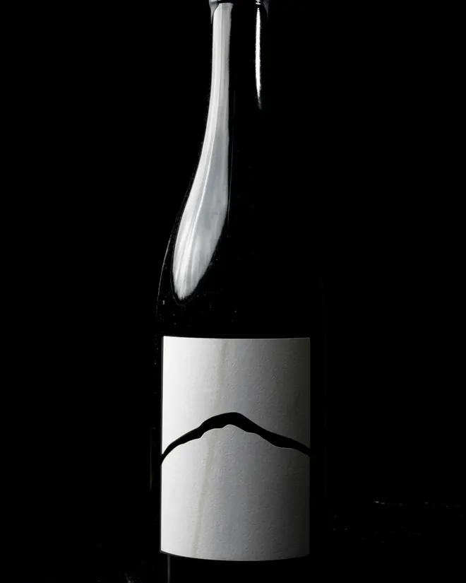 Botella negra con una etiqueta blanca que lleva el trazo de una montaña