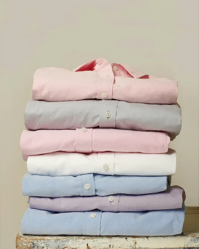 Pila de camisas dobladas de colores claros sobre un banco