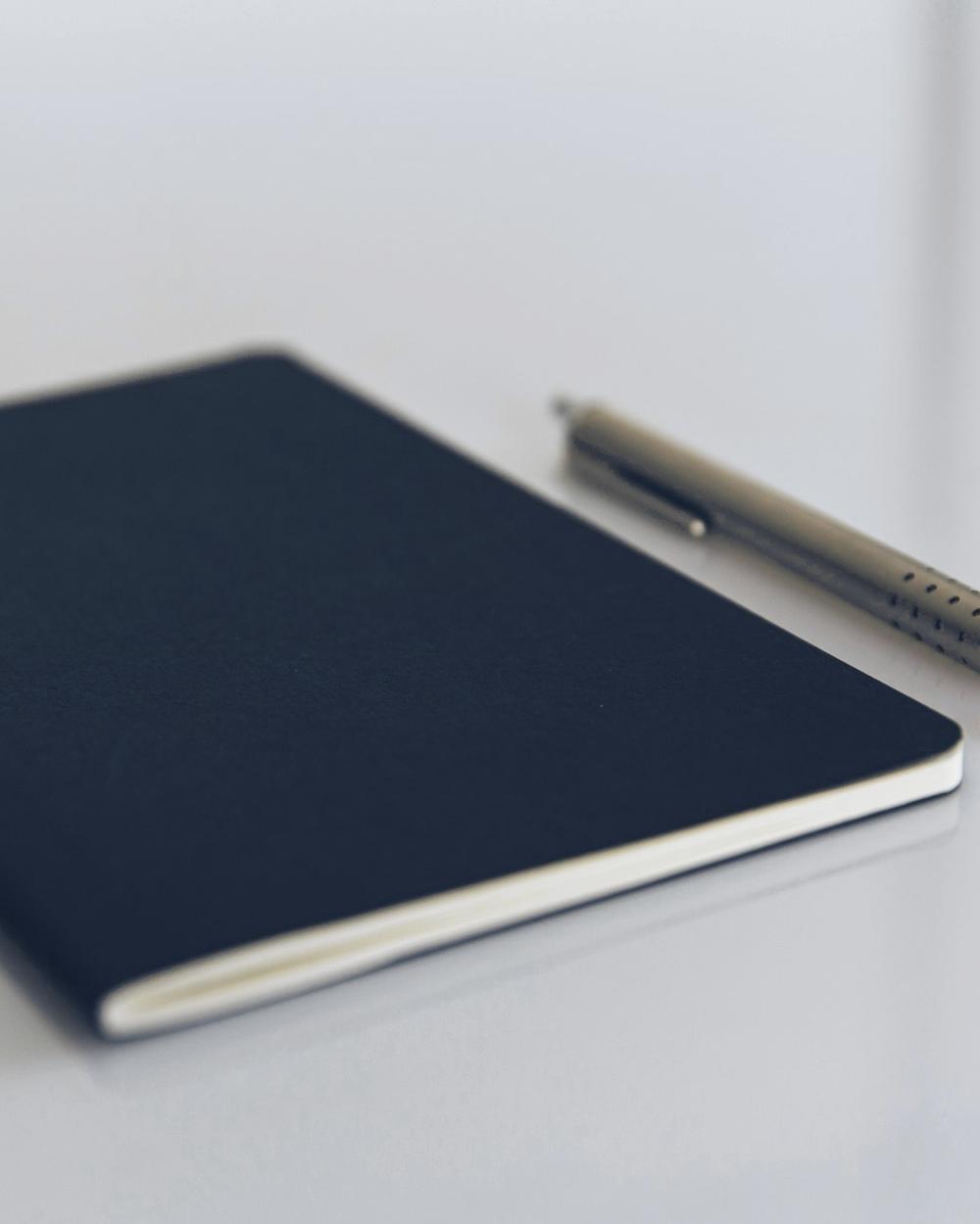 Libreta oscura y un bolígrafo de acero sobre una mesa clara