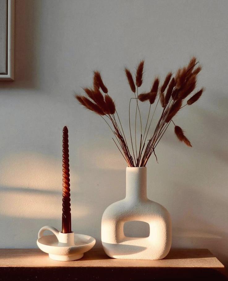 Repisa con un jarrón blanco, una vela roja y flores secas