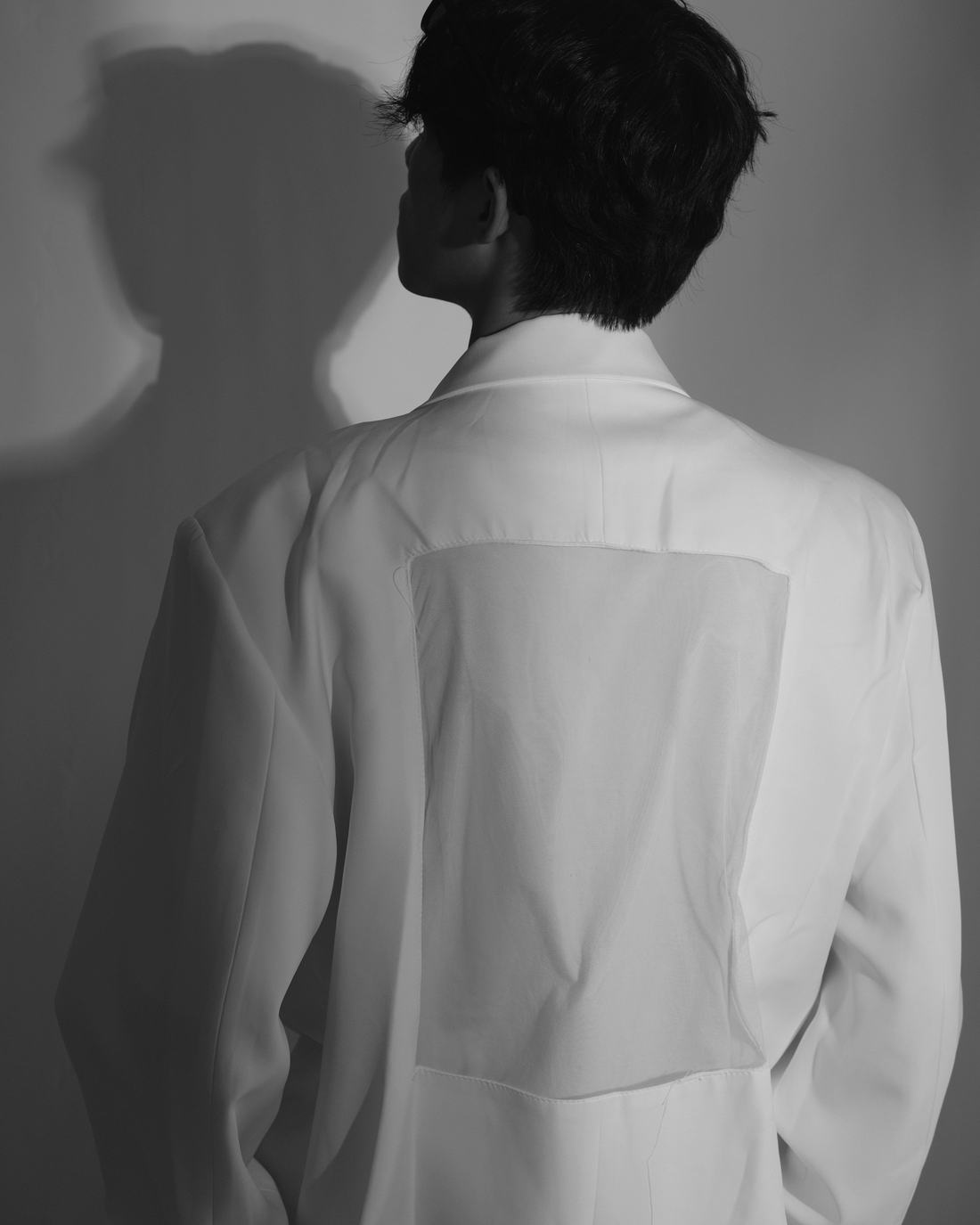 Una persona de espaldas con una chaqueta blanca amplia, junto a un muro gris