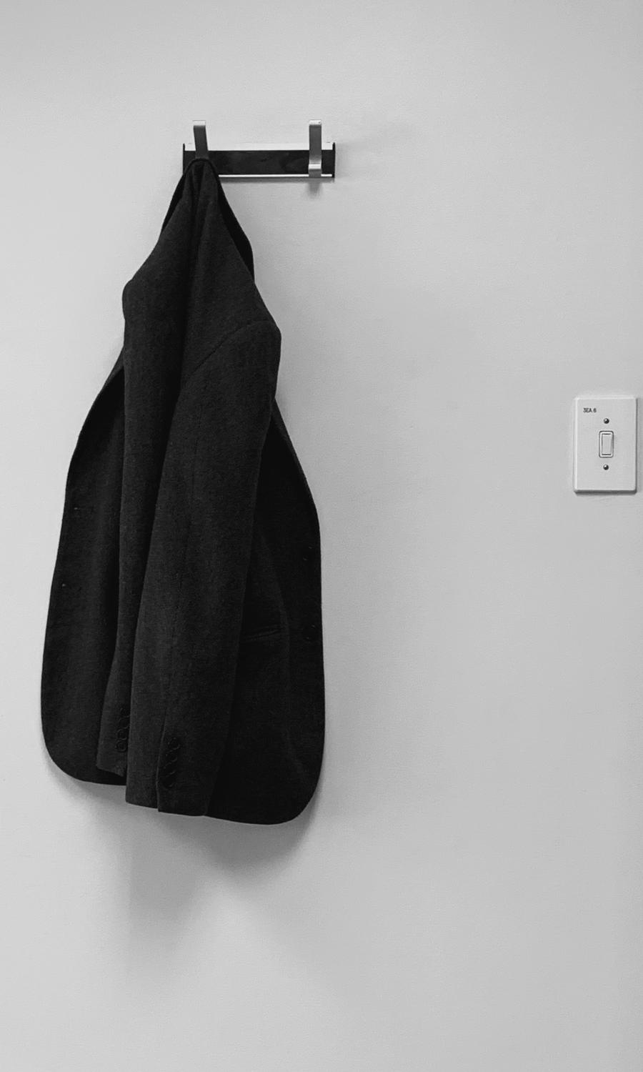 Un abrigo negro colgado de un gancho en una pared blanca