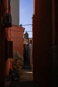 Calle en sombra con un campanario al fondo