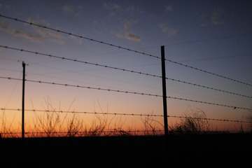 Alambre de púas y poste contra el atardecer