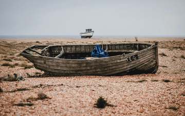Casco de madera varado en una playa de piedras, con otro bote lejano al fondo