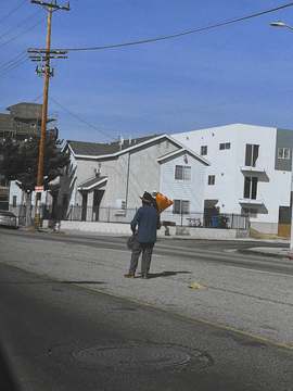 Figura de espaldas con un cono naranja bajo el brazo, en una calle vacía