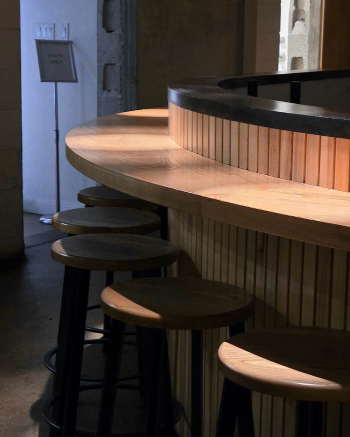 Barra curva de madera clara con taburetes altos en un café, con luz tenue