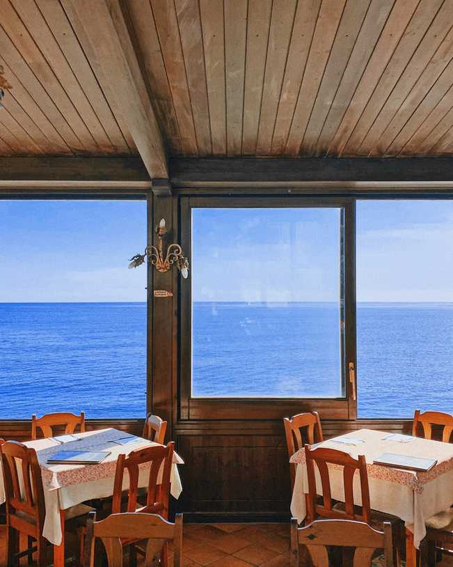 Comedor de madera con mesas puestas frente a una ventana que da al mar
