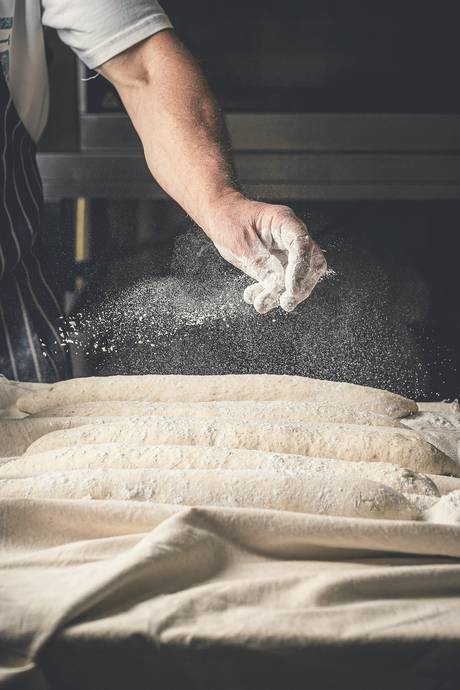 Una mano enharinando barras de pan en su lienzo