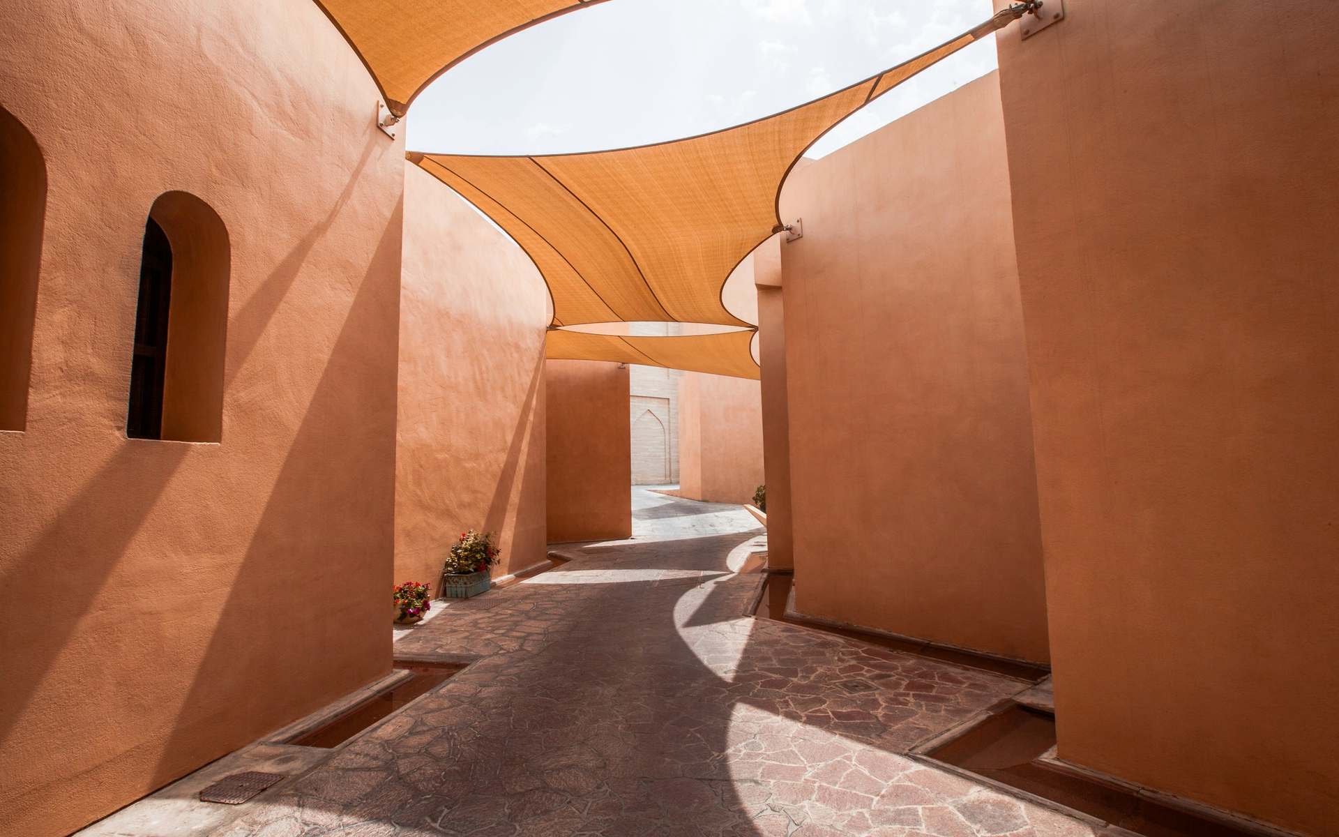 Pasaje de muros color terracota con un toldo que filtra la luz