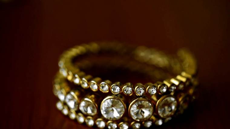 Un brazalete de oro con piedras claras sobre un fondo rojo oscuro