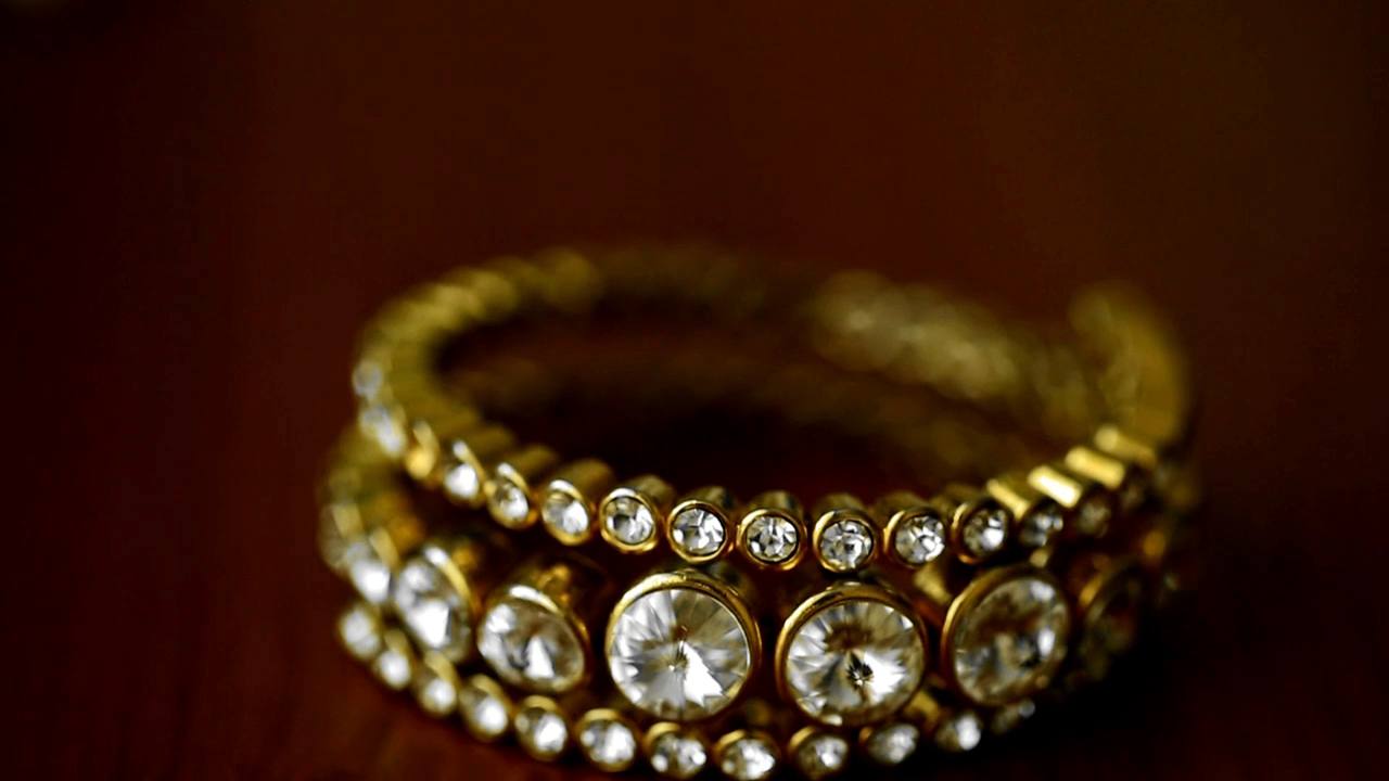 Un brazalete de oro con piedras claras sobre un fondo rojo oscuro, primer plano de la película de portada