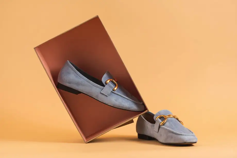 Mocasines lilas apoyados en un panel rojizo, sobre un fondo color durazno