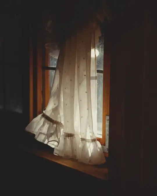 Vestido claro con volantes junto a una ventana, en una habitación en penumbra