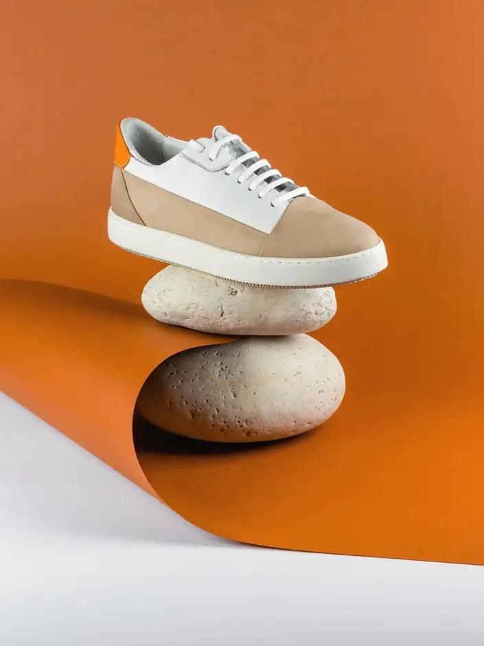 Zapatilla blanca y arena sobre dos piedras, con papel naranja de fondo