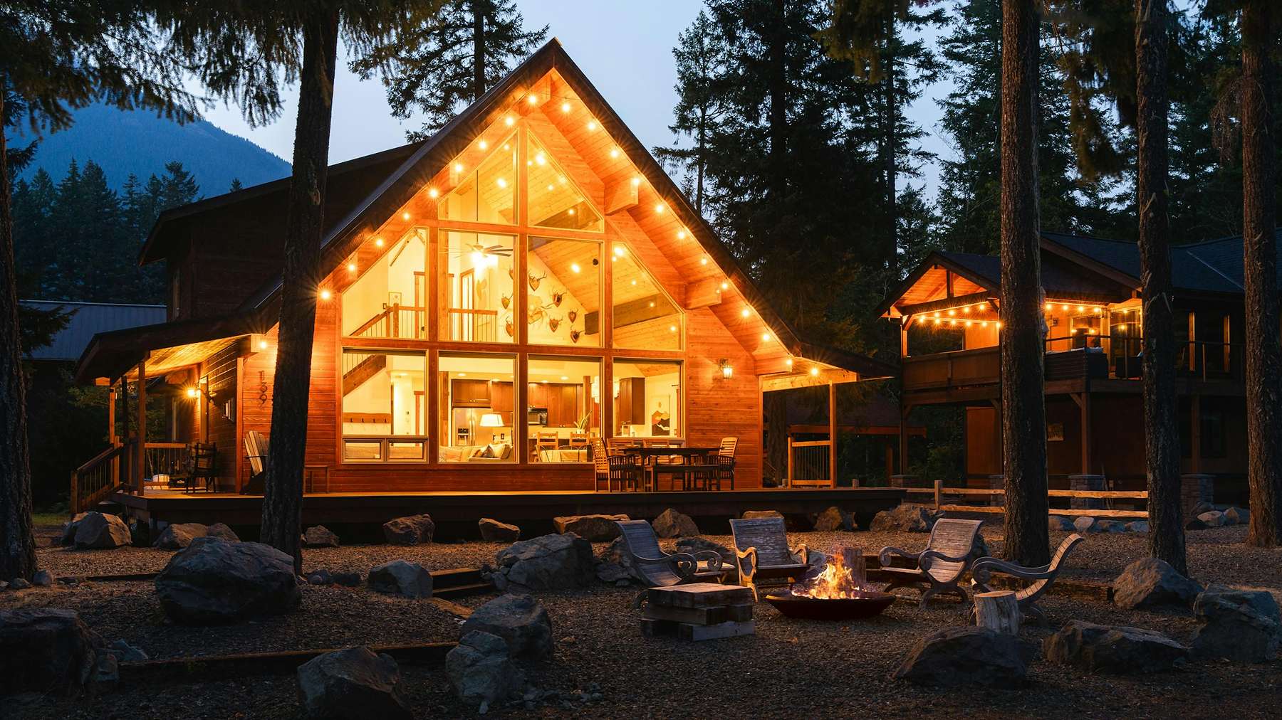 Refugio de madera con grandes ventanales iluminado al caer la tarde, entre pinos