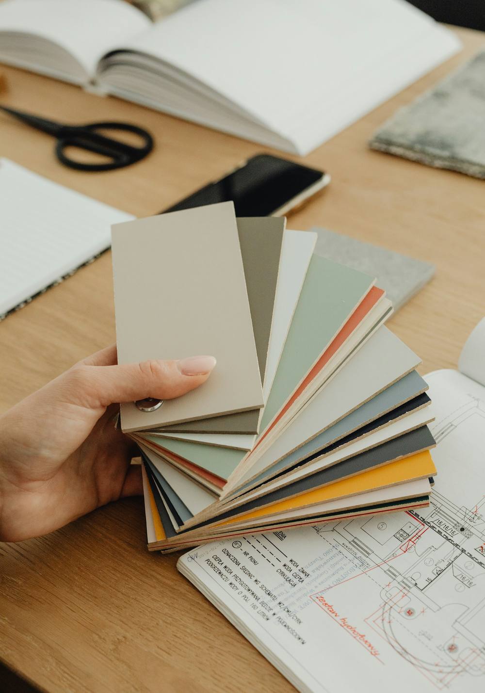 Manos con un abanico de muestras de papel y color, sobre planos y una mesa de trabajo