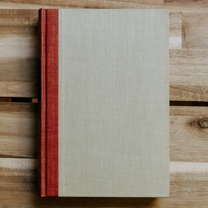 Libro de tela clara con lomo rojo sobre una mesa de madera