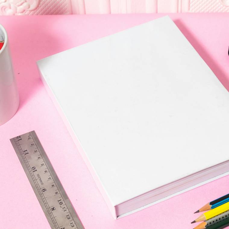 Catálogo de una muestra de grabado: libro de tapa blanca sobre papel rosa, junto a una regla y lápices