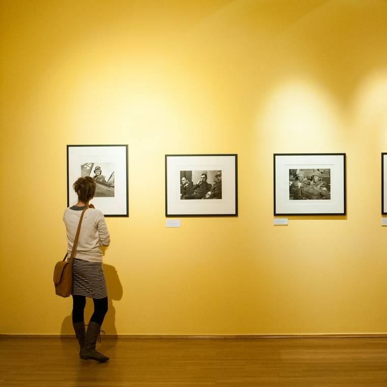 Gráfica de sala para una muestra de fotografía: sala de paredes amarillas con fotografías enmarcadas y una persona de espaldas