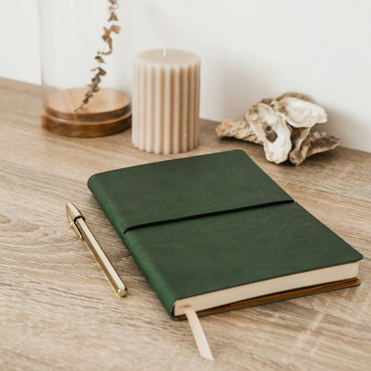 Cuaderno de tapa verde con cinta, junto a una campana de vidrio y una vela, para una colección de papelería
