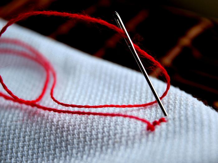 Aguja con hilo rojo sobre una tela clara