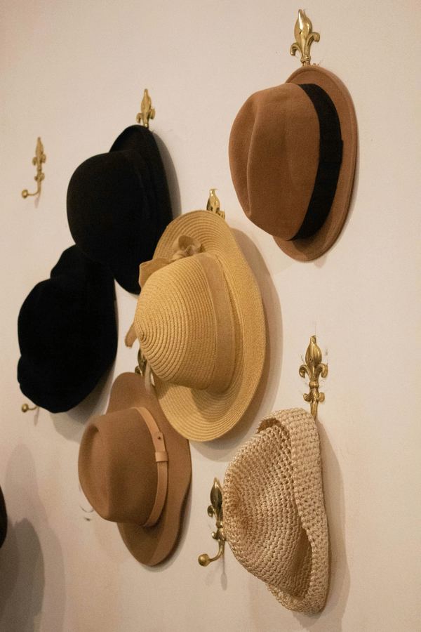 Sombreros de fieltro y paja colgados de ganchos dorados en una pared crema