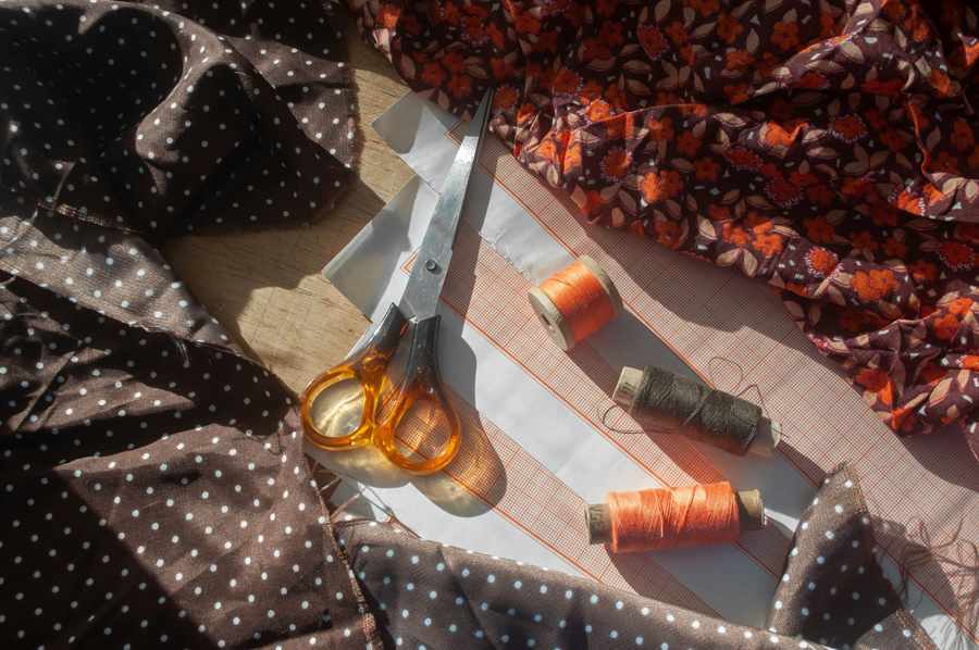 Tijeras, carretes de hilo y telas estampadas sobre una mesa de corte