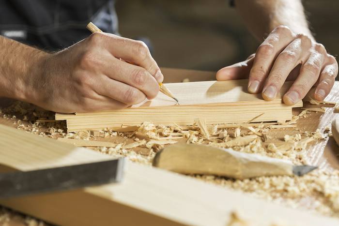 Manos marcando una tabla de madera rodeada de virutas