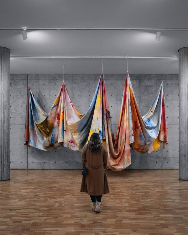 Telas de colores colgadas en una sala; una persona las mira de espaldas