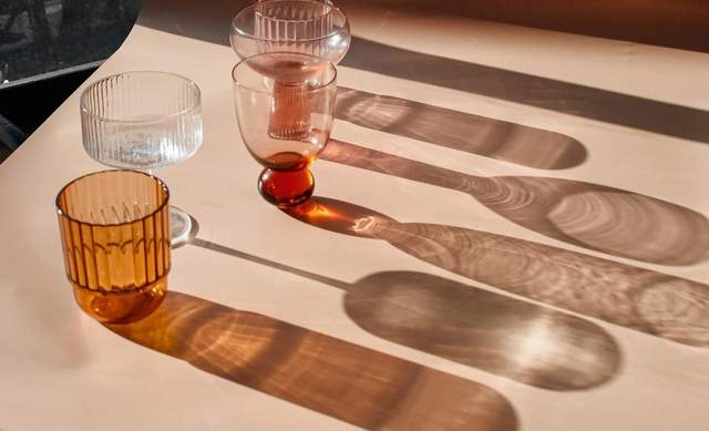 Copas y vasos de colores sobre una mesa, con sus sombras largas