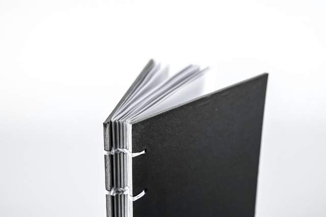 Libro de tapa negra con cosido visto, sobre fondo blanco