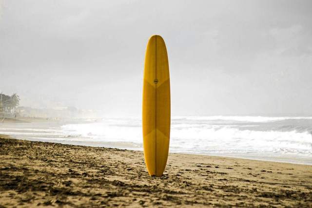 Tabla de surf amarilla clavada en la arena