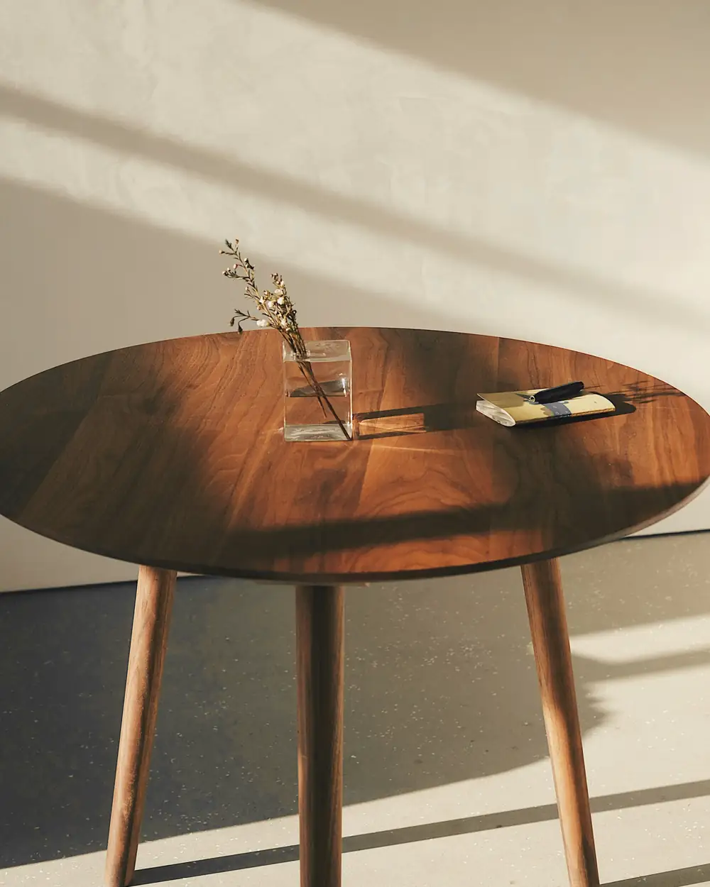 Mesa redonda de madera con tres patas, bañada por la luz de la tarde
