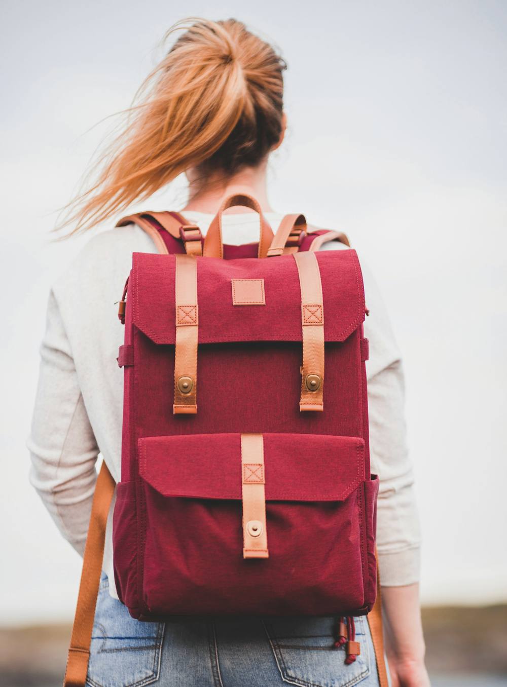 Mujer de espaldas con una mochila roja de lona y correas de cuero frente a un lago