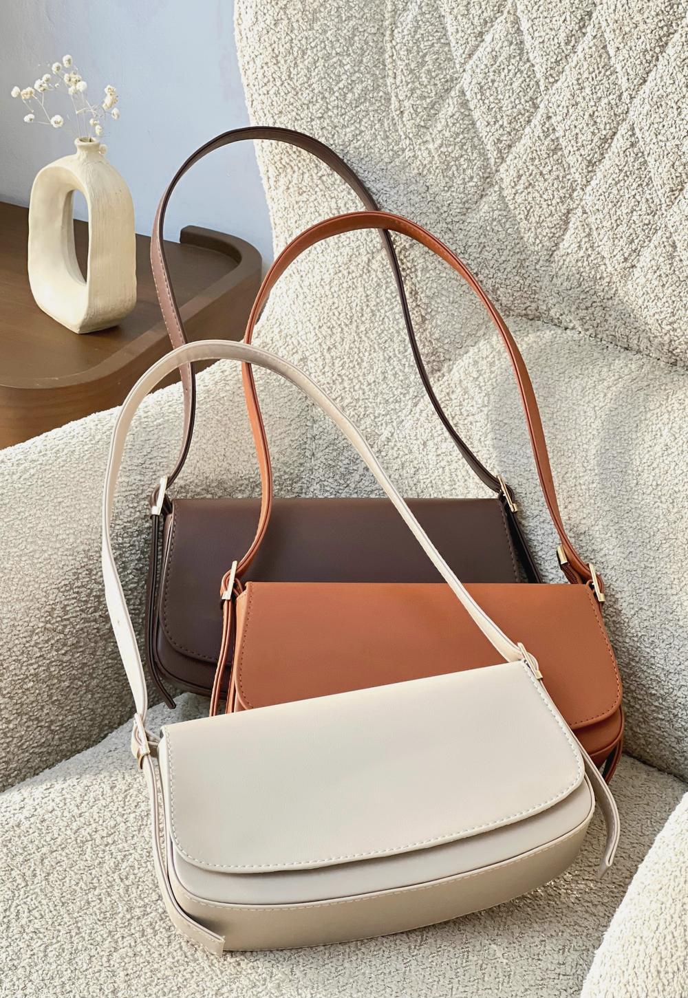Tres bolsos de cuero, crema, café y miel, sobre un sillón de bouclé
